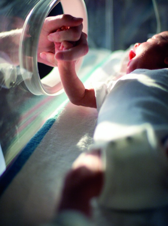 close up van een Kaukasische pasgeboren baby in een couveuse terwijl een verpleegster de baby bij de hand neemt